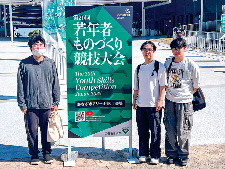 「第20回若年者ものづくり競技大会」の看板前に立つ参加学生3名