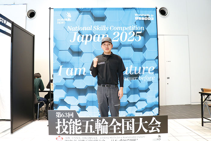 技能五輪全国大会の記念撮影ボード前でポーズをとる出場学生