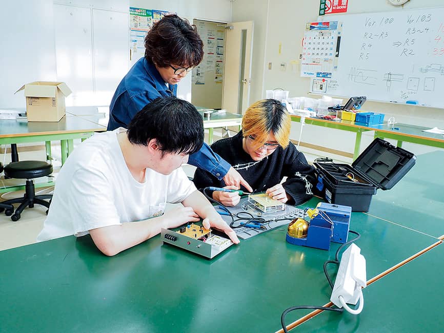 技能検定3級の対策練習で電子回路の実習に取り組む学生と指導する教員