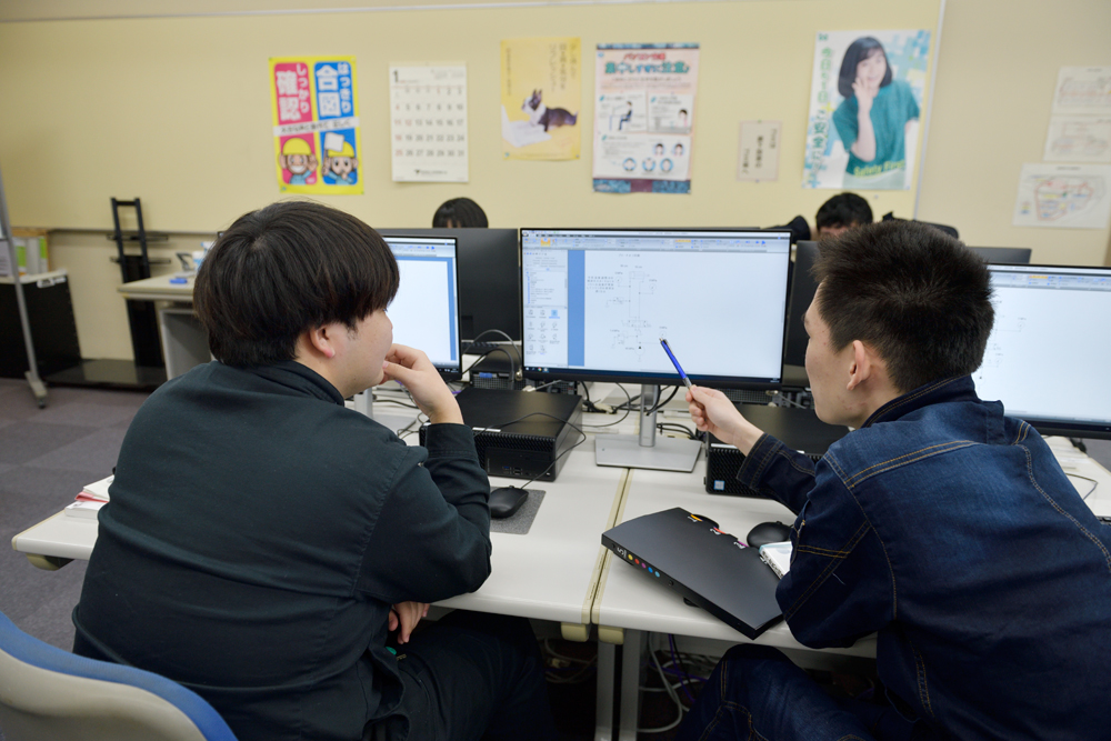 写真：３Ｄプリンタの前で制作物を手にする学生の様子